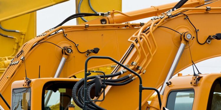 Gros plan sur des engins de chantier orange équipés de bras hydrauliques et de tuyaux noirs.