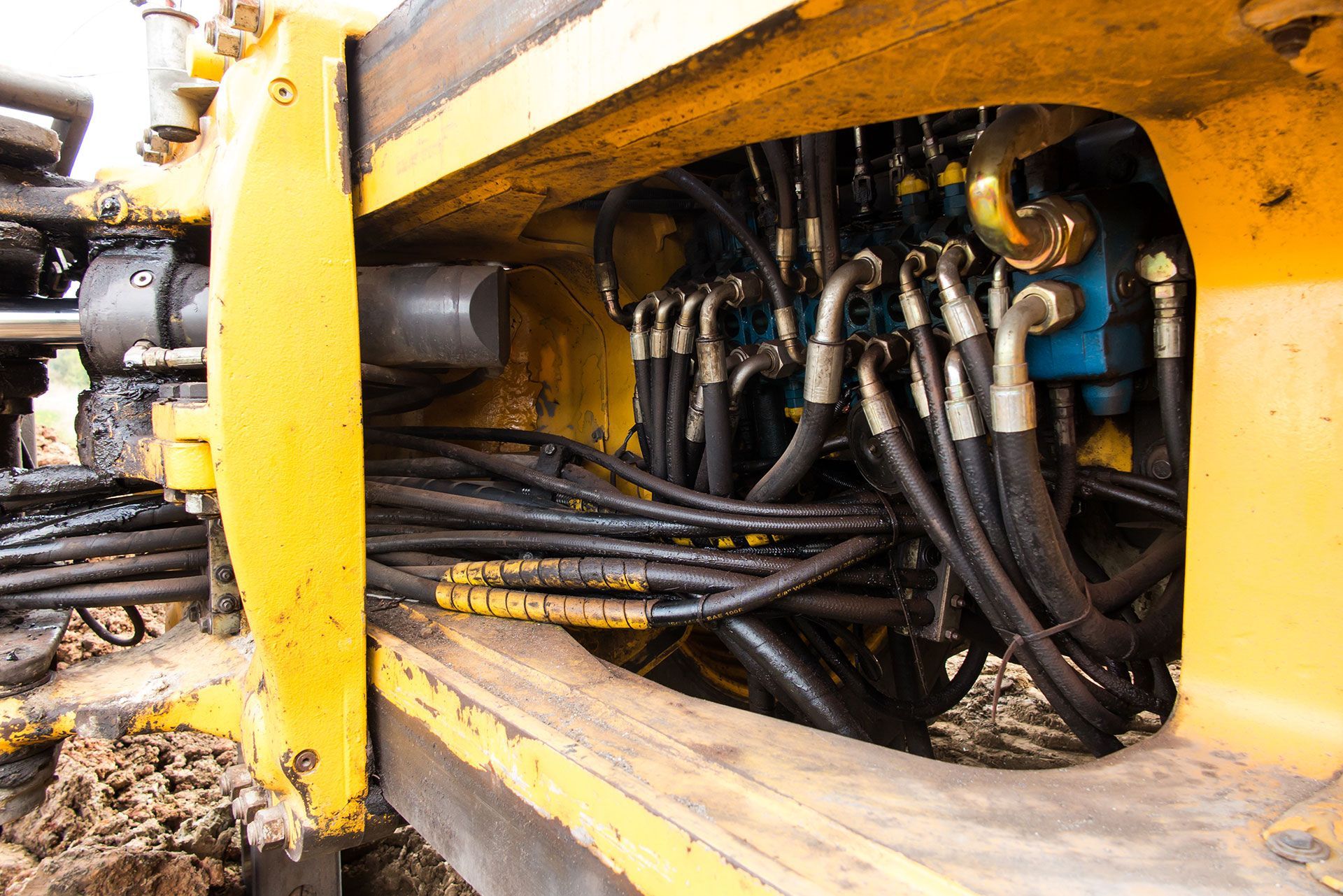 Gros plan sur une machine industrielle jaune avec des tuyaux hydrauliques noirs enchevêtrés et des raccords métalliques à l'intérieur d'un compartiment