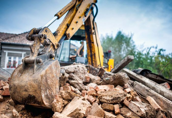 Godet d'une excavatrice soulevant des gravats sur un chantier de démolition jonché de briques cassées et de débris.