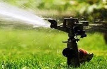 Un aspersor está rociando agua sobre un césped verde y exuberante.