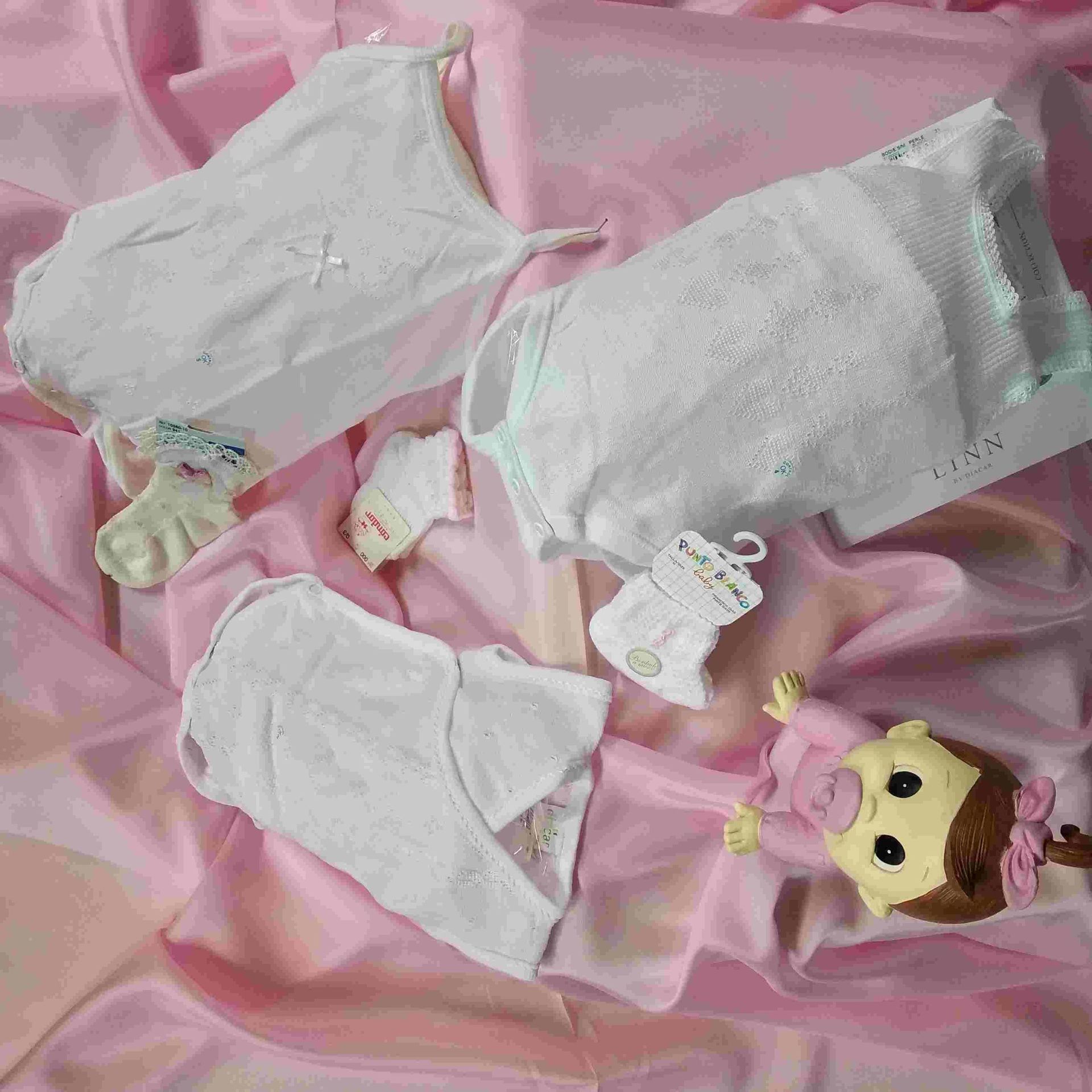 Una muñeca está acostada en una cama con ropa y un chupete.