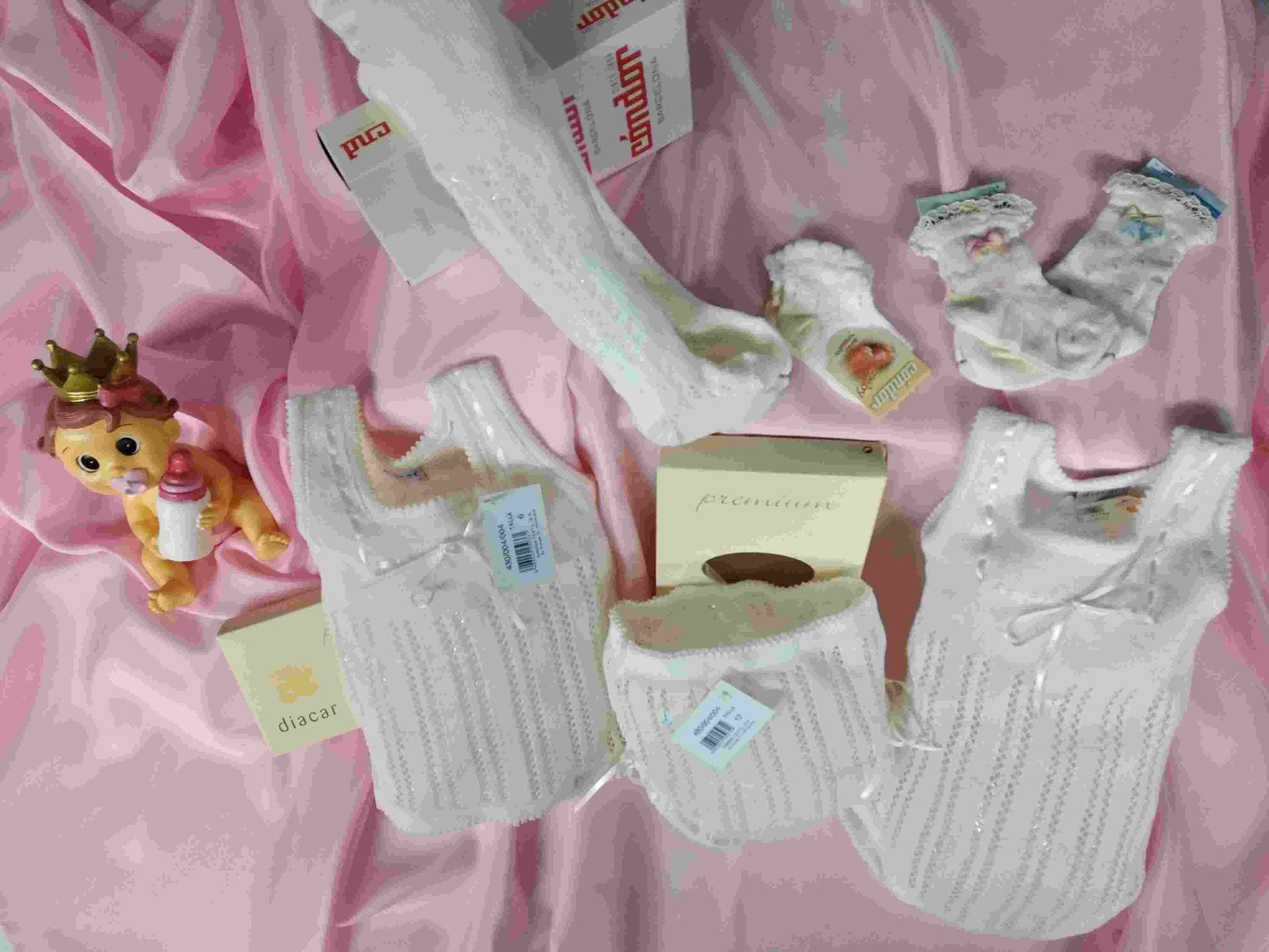 Un montón de ropa de bebé está colocada sobre una tela rosa.