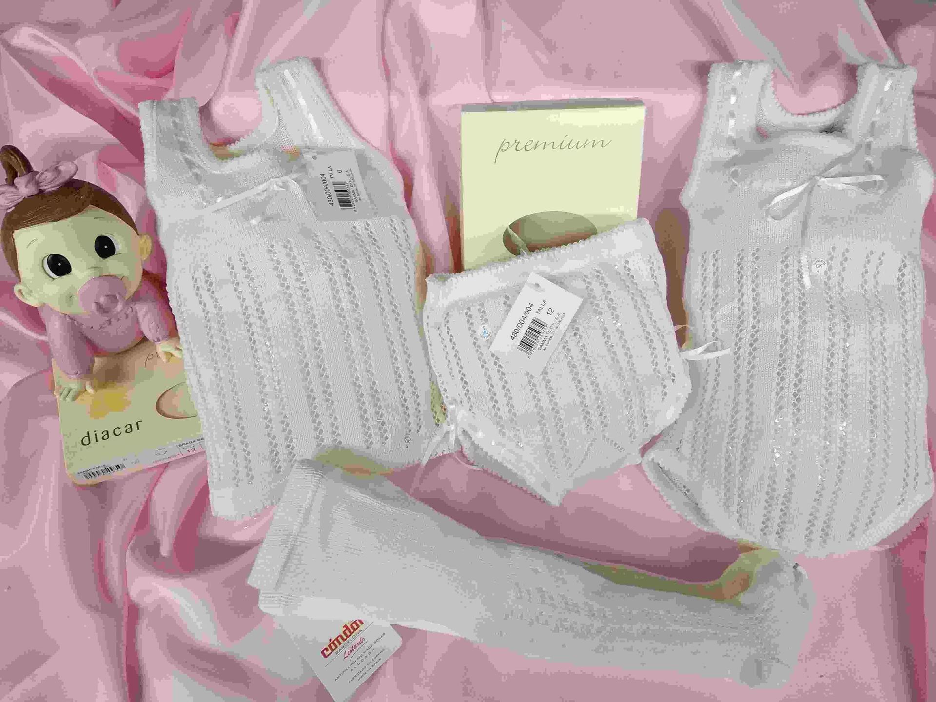 Una muñeca con un chupete está sentada junto a una pila de ropa de bebé.