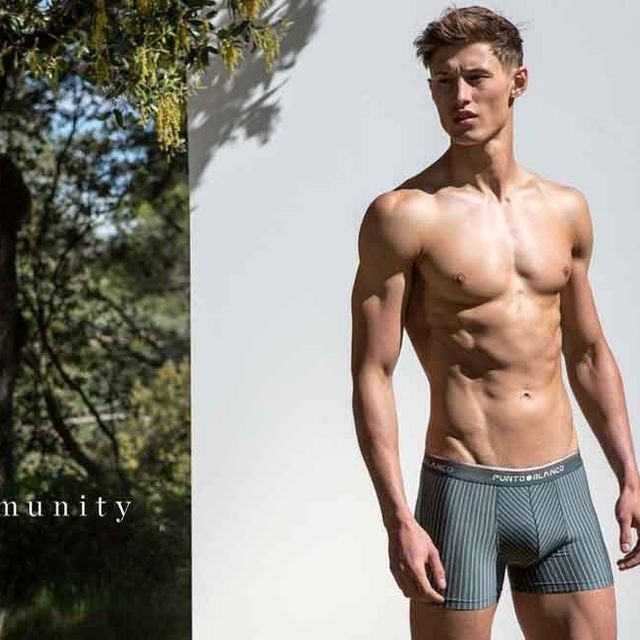 Un hombre sin camisa y en calzoncillos está parado frente a un árbol.