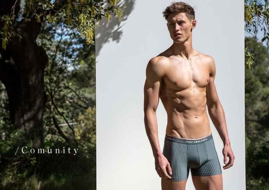 Un hombre sin camisa y en calzoncillos está parado frente a un árbol.