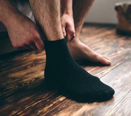 Un hombre se ata los calcetines negros en un suelo de madera.