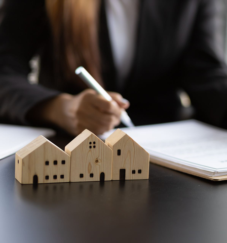 Des maquettes de maisons en bois sont disposées devant une personne signant des documents à un bureau.