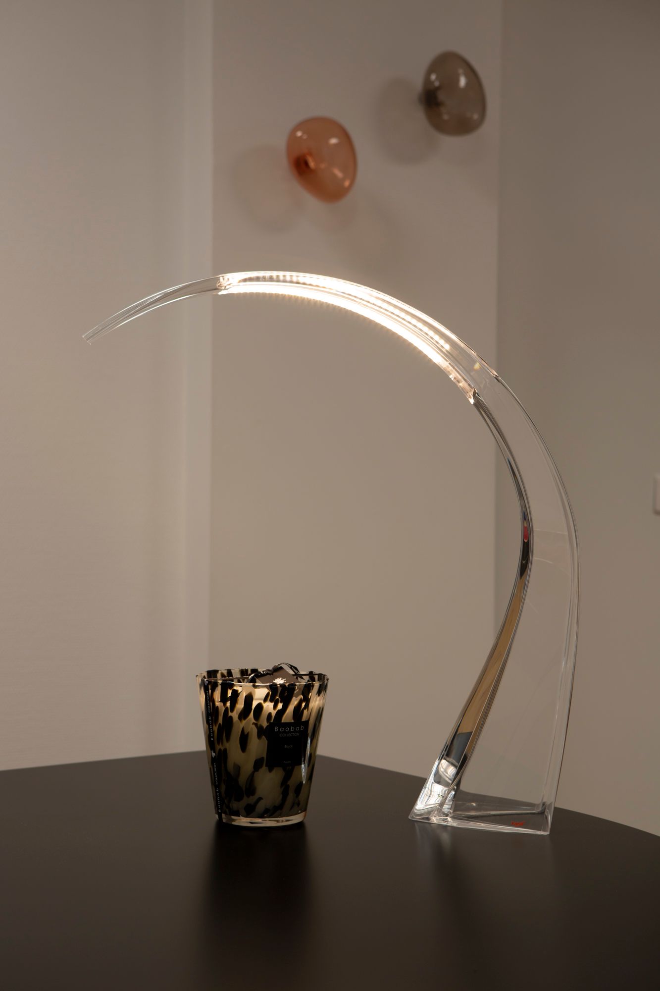 Lampe argentée incurvée sur une surface, à côté d'un bougeoir, devant un mur.