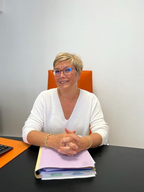 Femme assise à un bureau, souriante, les mains jointes sur un dossier.
