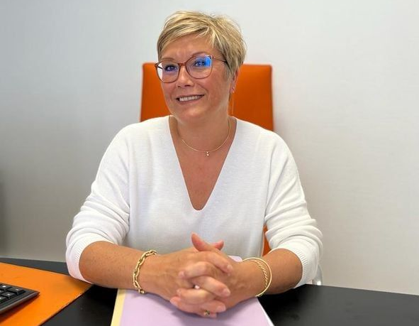 Femme souriante assise à un bureau, les mains jointes.