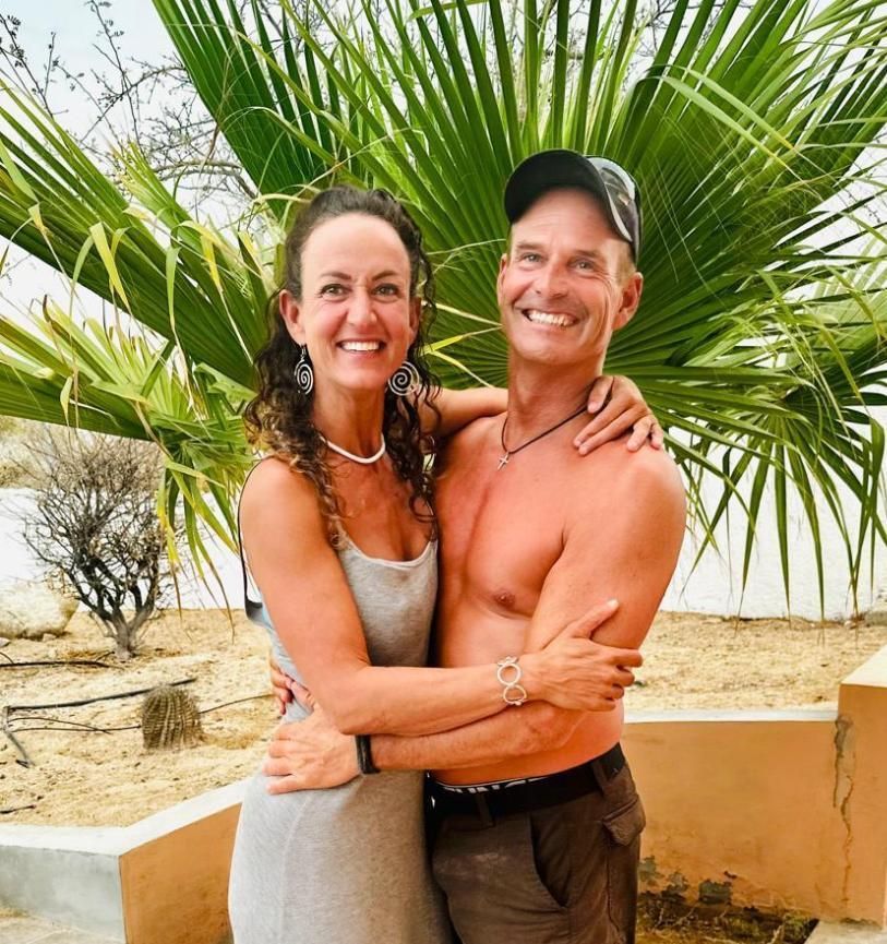 A man and a woman are posing for a picture in front of a palm tree.