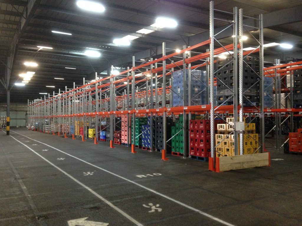Grand entrepôt avec de longues rangées d'étagères de stockage orange et argent sous des plafonds lumineux.