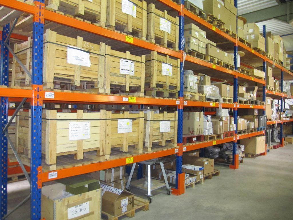 Allées d'entrepôt avec des cartons empilés sur des étagères industrielles orange et bleues.