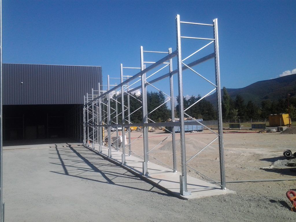 Échafaudage métallique dans un chantier extérieur ensoleillé, à côté d'un bâtiment sombre et d'une montagne en arrière-plan.