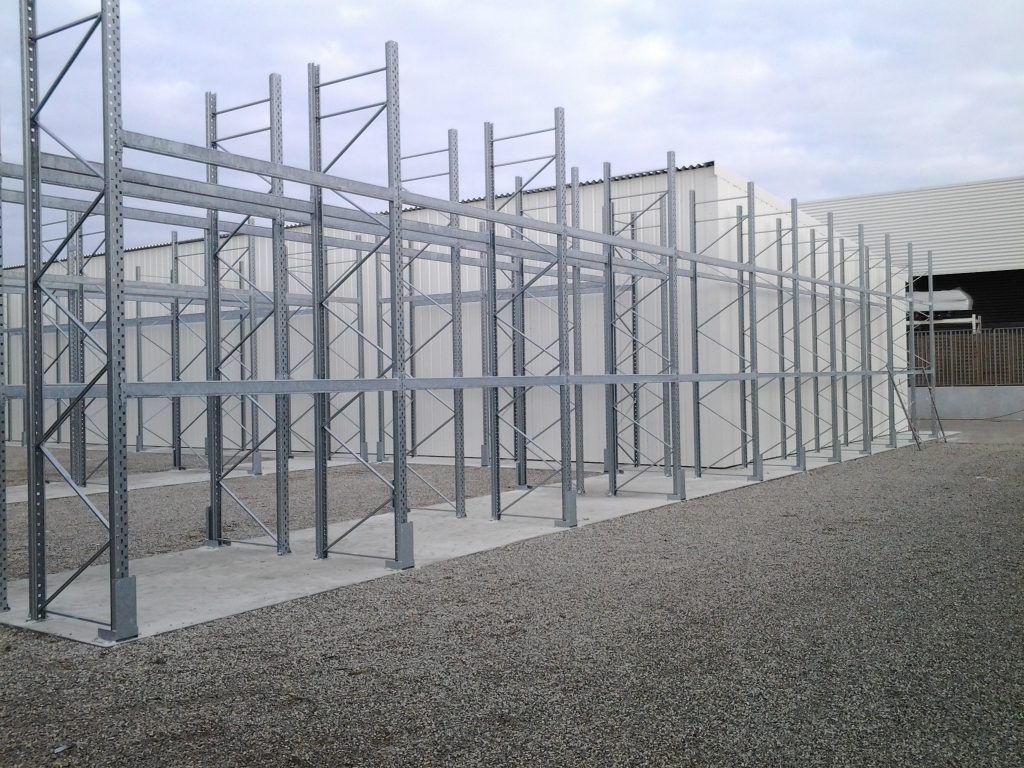 Rayonnages métalliques vides dans une aire de stockage industrielle extérieure au sol gravillonné.