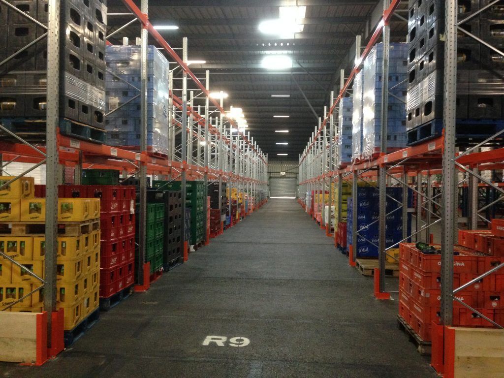 Allée d'un entrepôt avec de hauts rayonnages à palettes chargés de cartons et de caisses des deux côtés