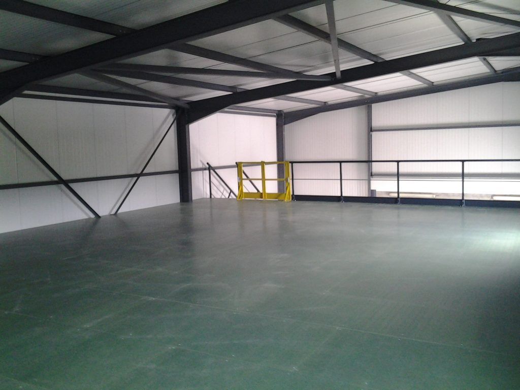 Intérieur d'entrepôt industriel vide avec poutres métalliques et sol vert