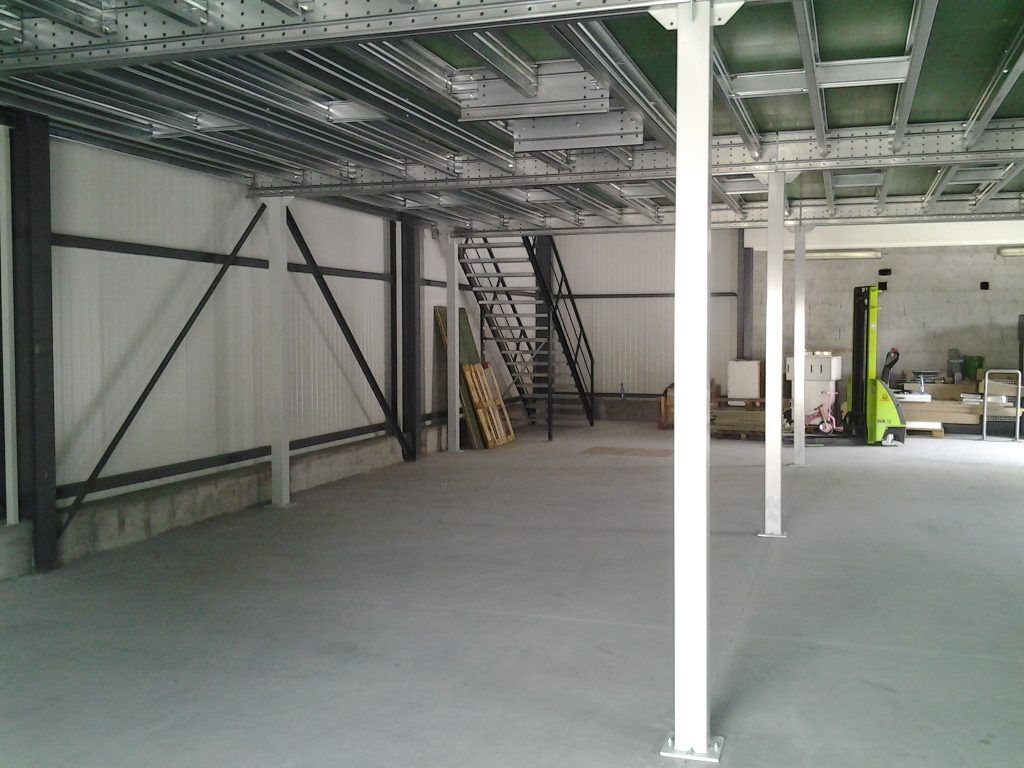 Intérieur d'un entrepôt industriel vide avec sol en béton, poutres métalliques, escaliers et colonnes de soutien