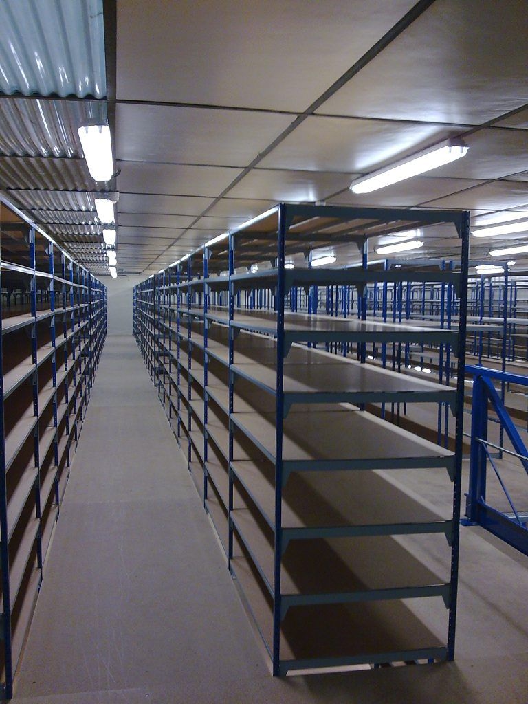 Allée d'entrepôt vide avec des étagères métalliques bleues de chaque côté et des néons au plafond