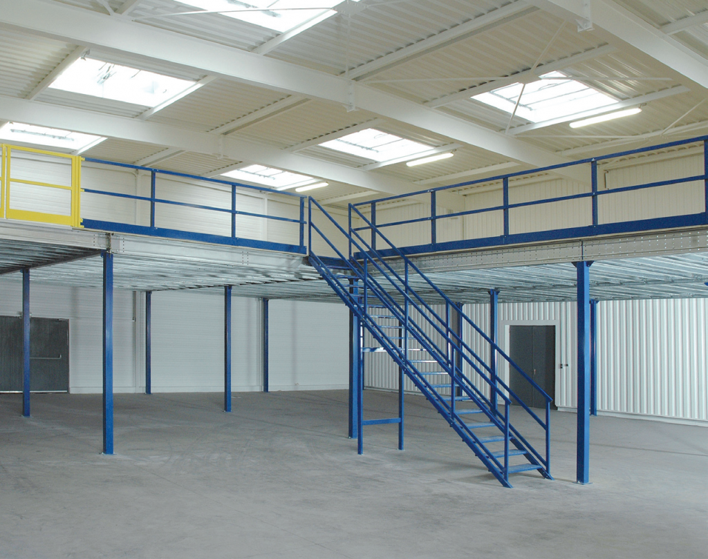 Loft industriel vide avec mezzanine en métal bleu et rambarde sous un plafond blanc