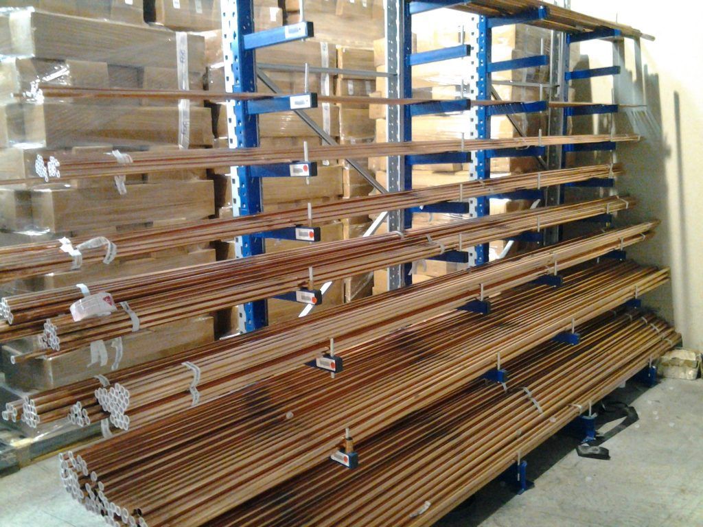 De longues lattes de bois empilées sur des étagères métalliques bleues dans un entrepôt ou un atelier.