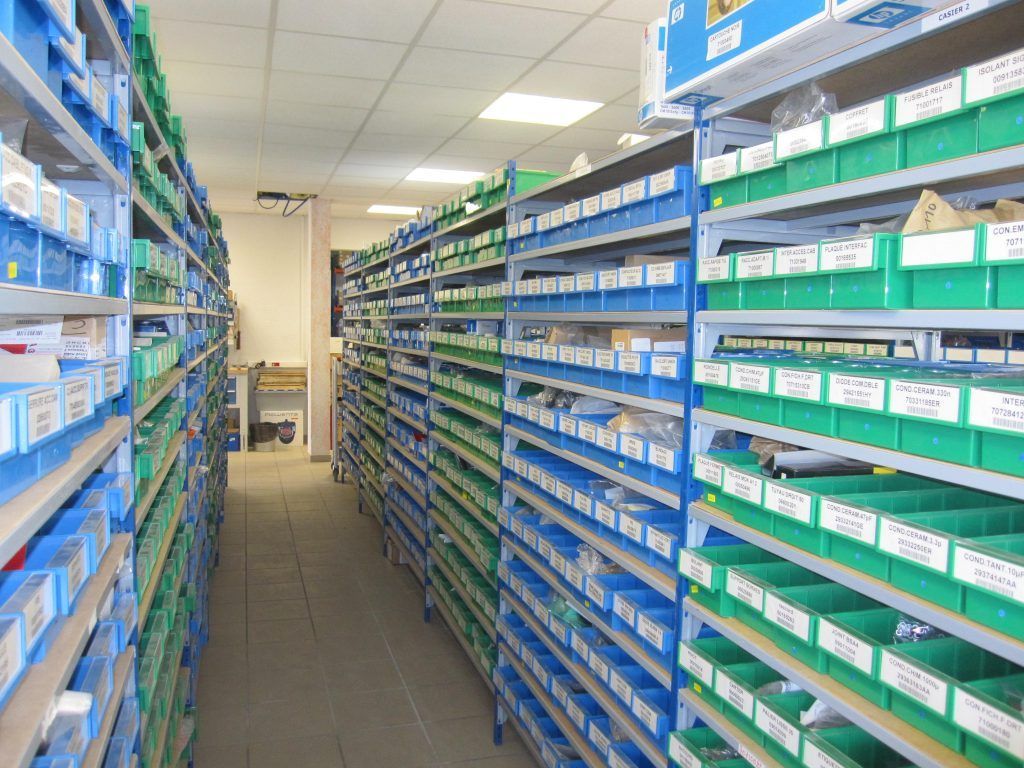 Un rayon de pharmacie avec des étagères bleues et vertes remplies de médicaments et de fournitures en boîtes.