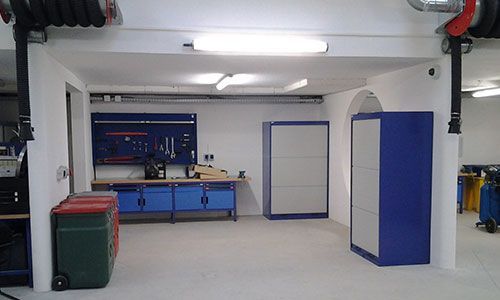 Atelier lumineux dans un garage, avec établi bleu, outils, armoires et bacs sous éclairage fluorescent.