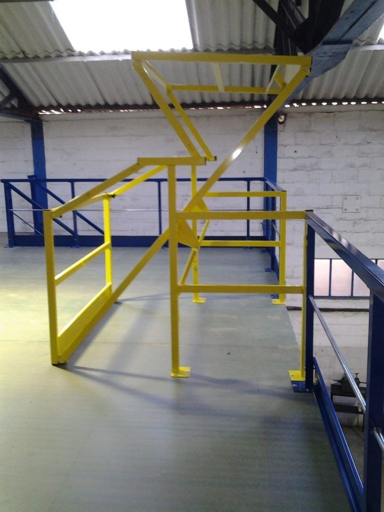 Portail de sécurité et rambardes en métal jaune sur une passerelle intérieure de mezzanine industrielle.