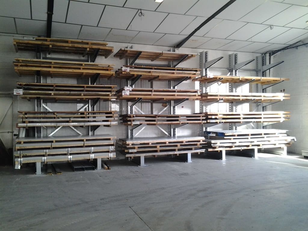 Entrepôt vide avec des étagères métalliques chargées de longues planches le long du mur