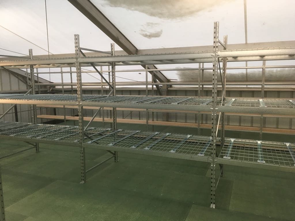 Pièce industrielle vide avec des étagères métalliques et un revêtement de sol vert sous un plafond en bâche