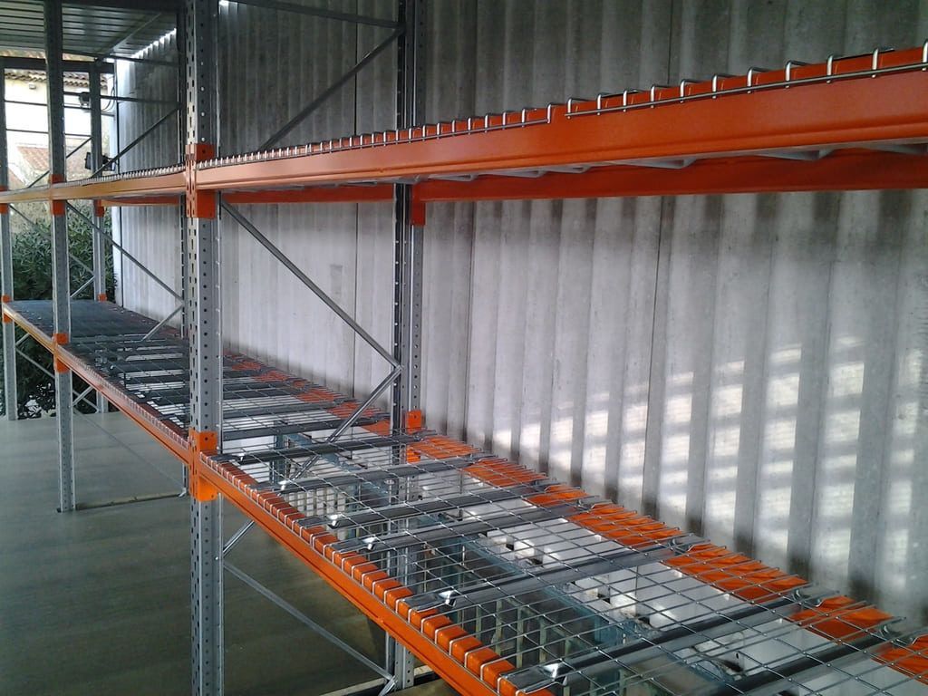Rayonnages industriels vides dans un entrepôt, avec des poutres orange et des étagères en fil métallique.