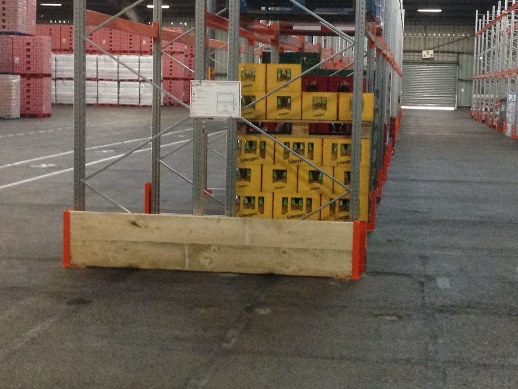 Allée d'entrepôt avec des cartons jaunes empilés derrière une barrière rouge et métallique et un grand bloc de bois.