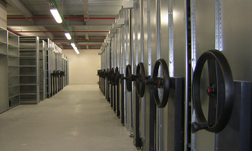 Allée de grande salle serveur avec des rangées de baies métalliques et des vannes à roue noires sur le mur de droite