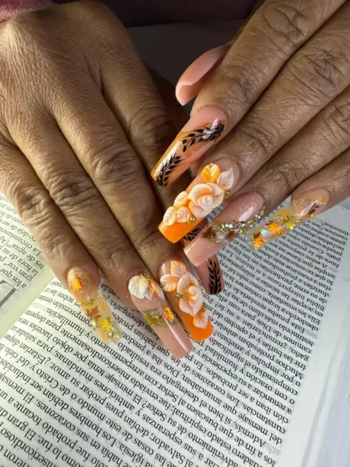 Manos con uñas decoradas con motivos florales de color naranja, apoyadas sobre la página de un libro.