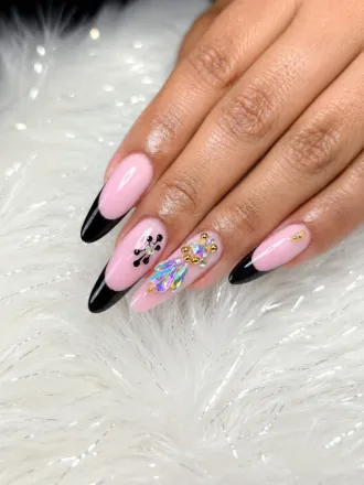 Mano con uñas acrílicas rosas y negras y detalles de purpurina sobre un fondo de piel blanca.