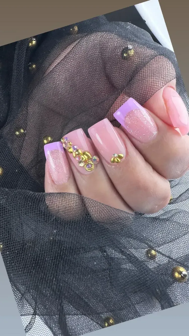 Mano con uñas pintadas con punta francesa y purpurina rosa, y detalles dorados, apoyada sobre tela de malla negra transparente.