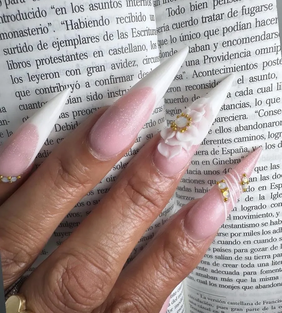 Mano con uñas largas de color rosa, una uña blanca con forma de flor, apoyada sobre la página impresa de un libro en español.