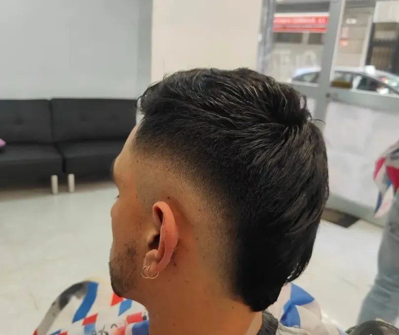 Vista lateral de un corte de pelo corto con degradado y la parte superior oscura, mostrado en una silla de barbero.