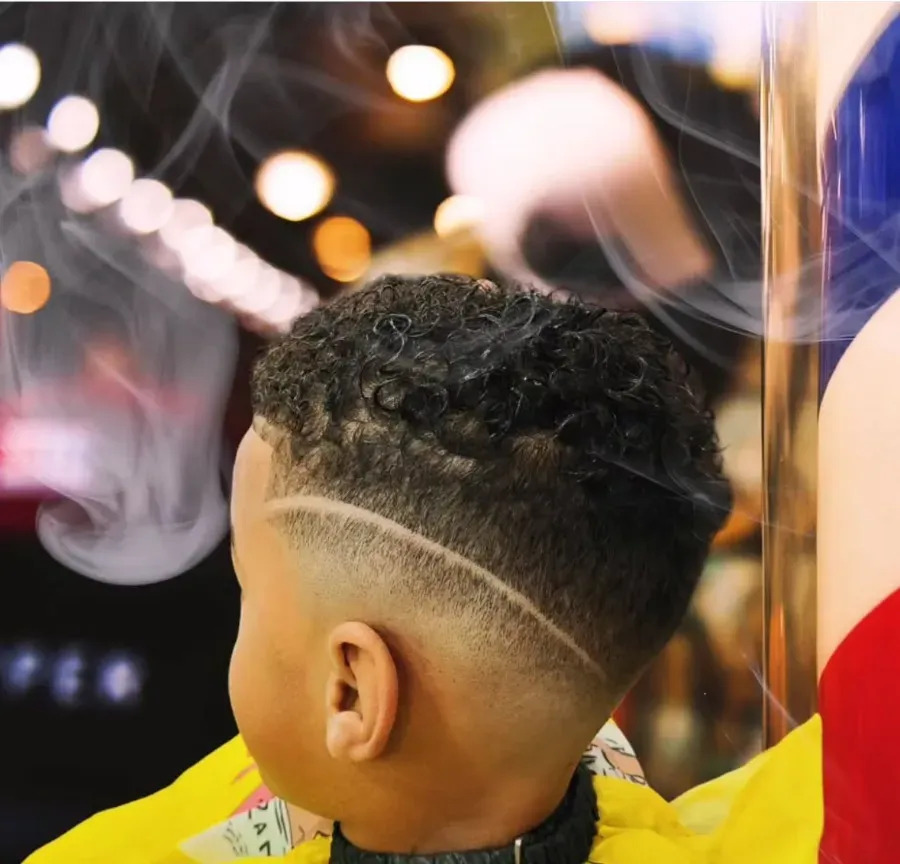 Corte de pelo rizado con los lados descoloridos y un diseño de línea rapada, visto desde atrás en el espejo de una peluquería.
