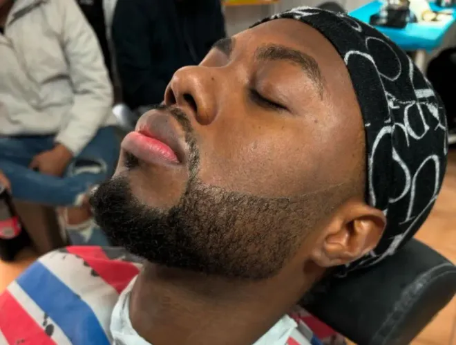 Hombre recostado con los ojos cerrados, vistiendo un pañuelo negro estampado en la cabeza y una camisa a rayas rojas, blancas y azules.