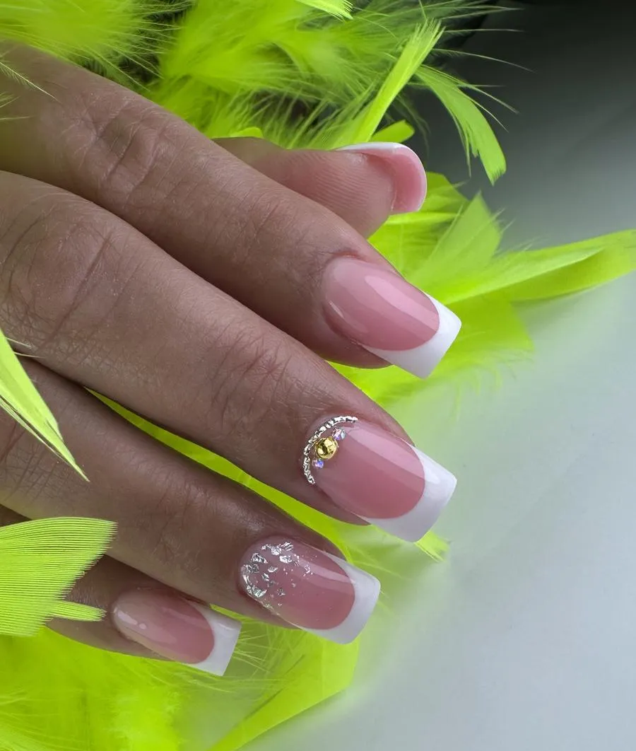 Mano con manicura francesa rosa y uñas decoradas con pedrería sobre plumas de color verde neón brillante.