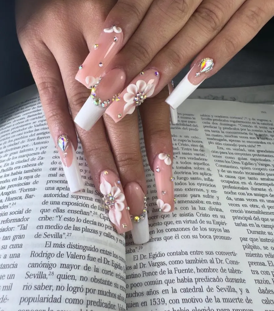 Uñas acrílicas largas de color rosa con estampado floral sobre la página de un libro abierto.