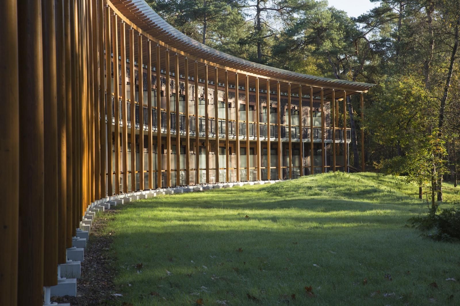 A curved wooden fence surrounds a lush green field in front of a building.