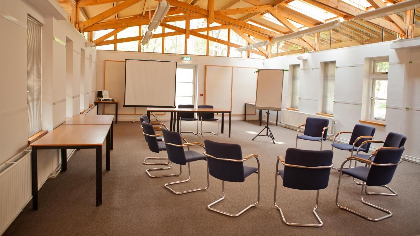 A conference room with tables and chairs and a projector screen