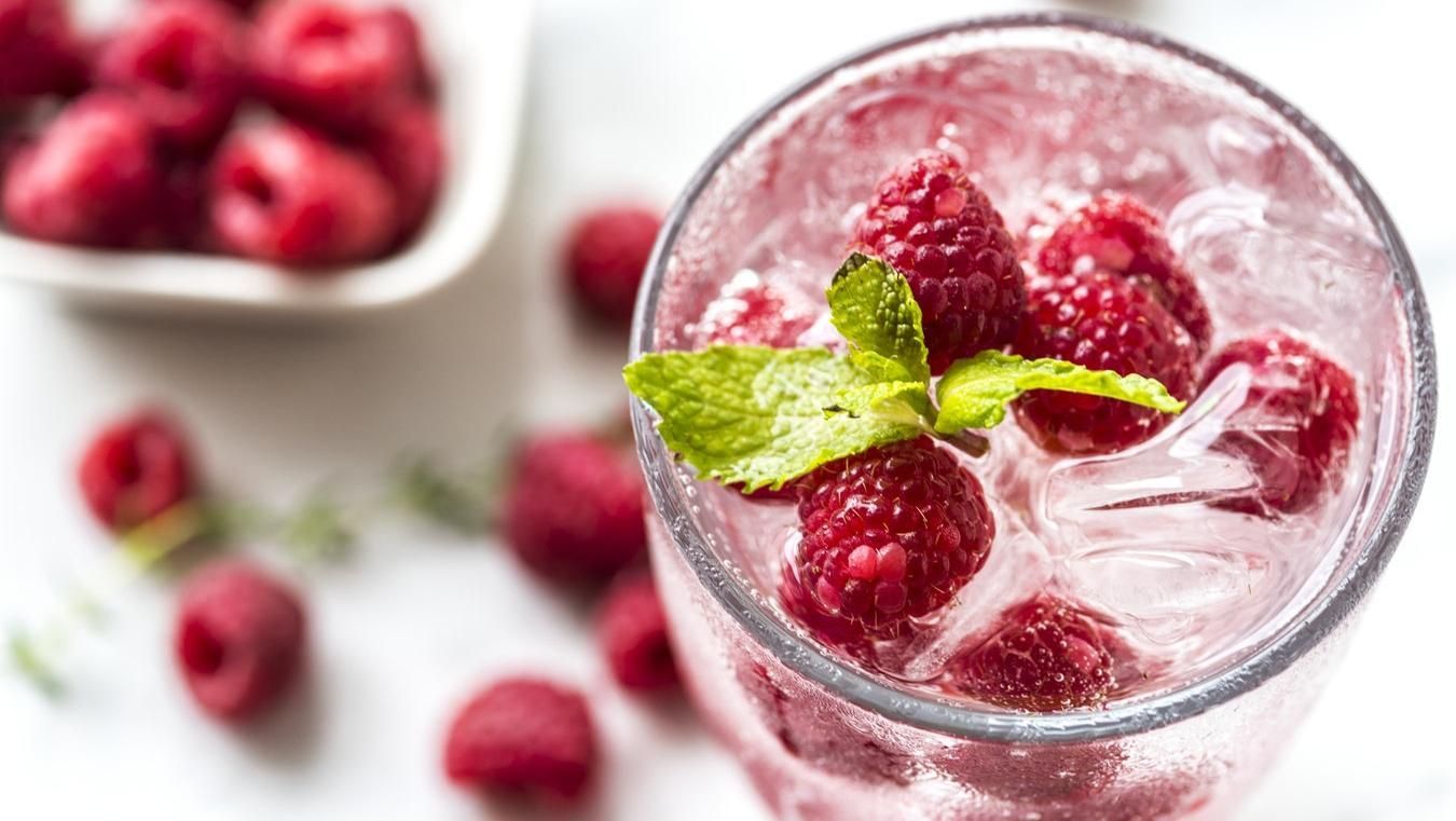 A glass of water with raspberries and mint leaves in it.