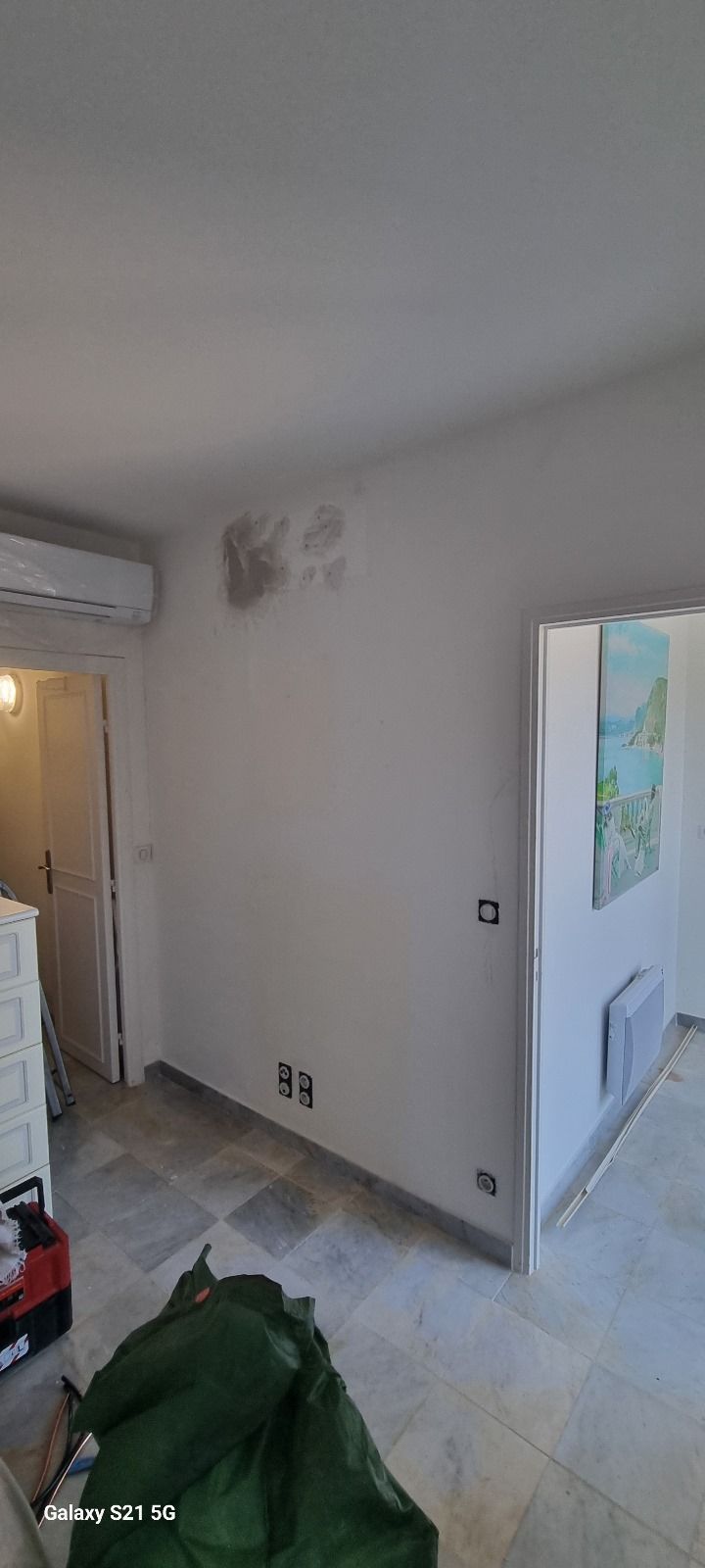 Une pièce avec des murs blancs et un sac vert sur le sol.