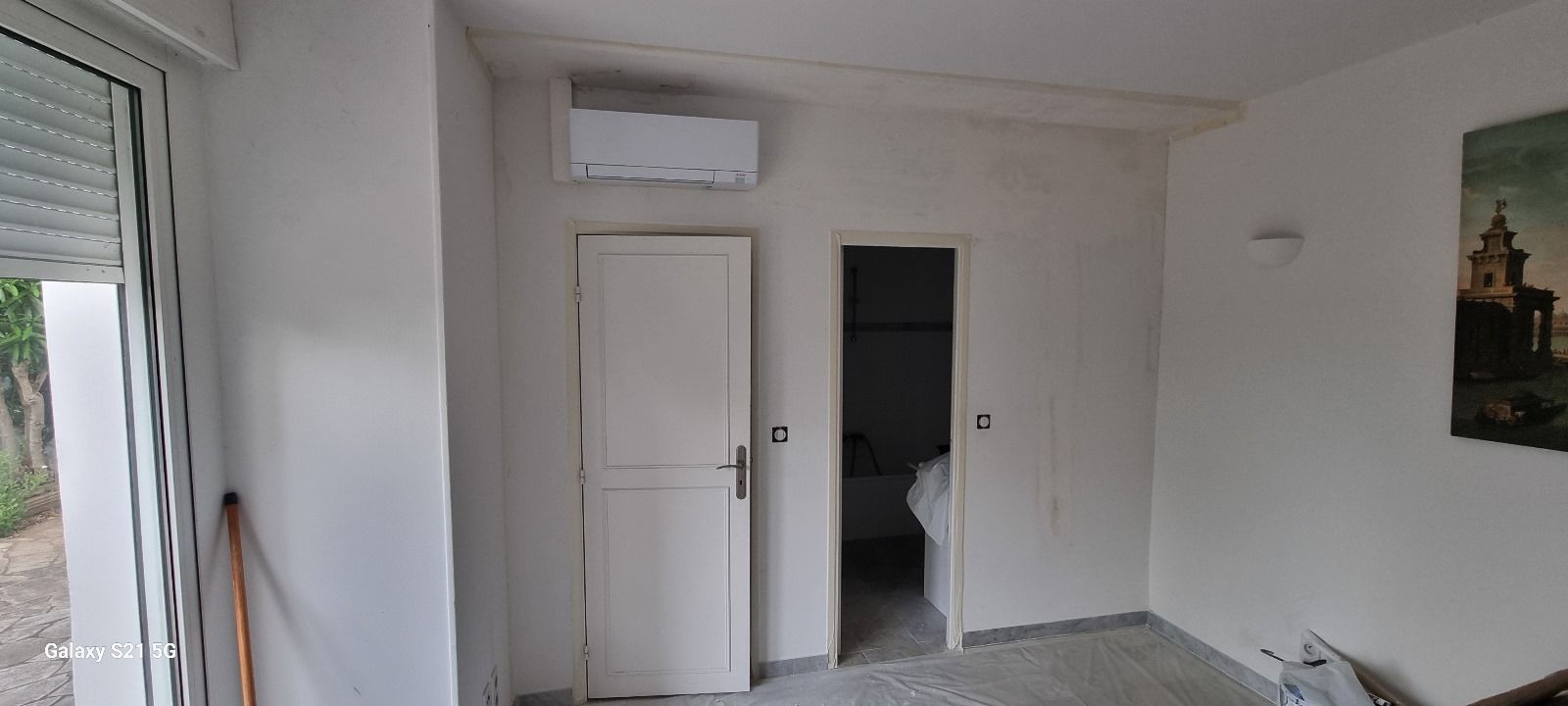 Une pièce avec une porte et une fenêtre avec un tableau sur le mur.