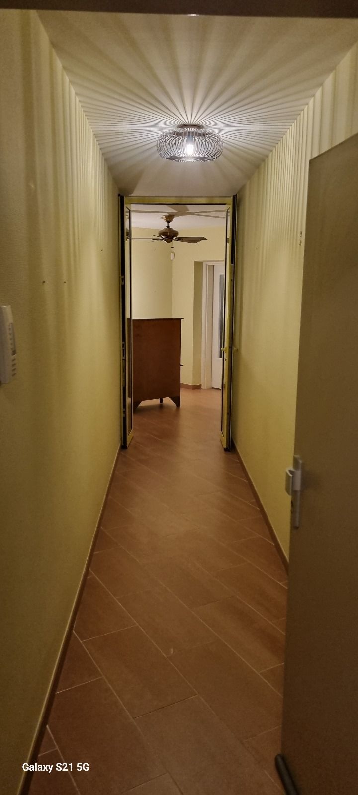Un long couloir avec un ventilateur de plafond et une porte menant à une pièce.