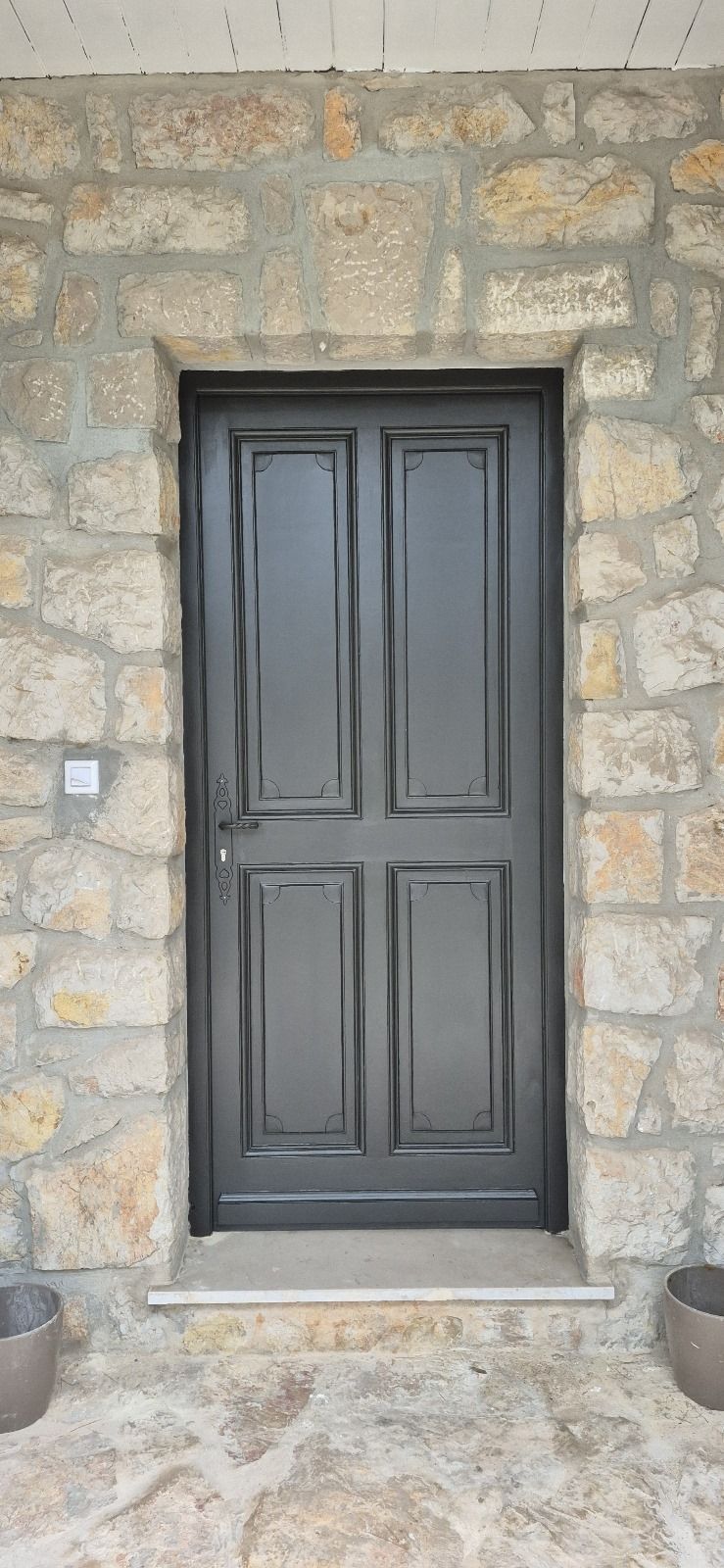 Une porte noire se trouve devant un mur de pierre.