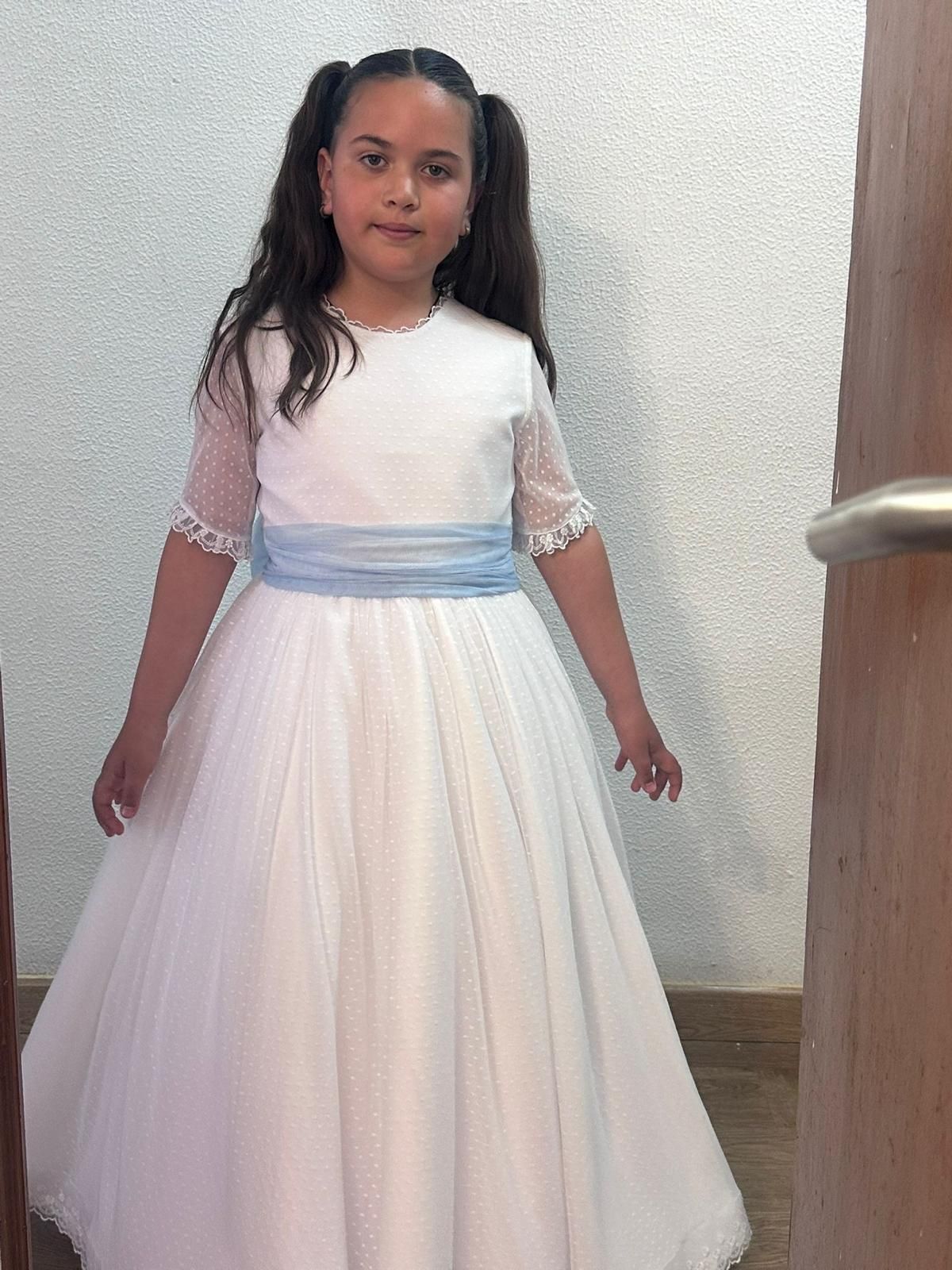 Una niña con un vestido blanco está parada frente a una puerta.